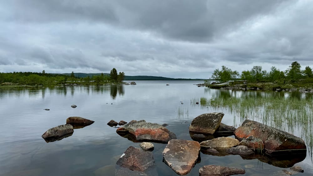 a lake with ripples and a shoreline of large rocks.
