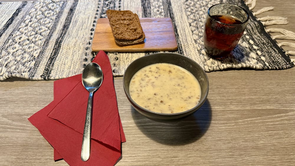 A bowl of soup is sitting on a table next to a spoon and a glass of wine.