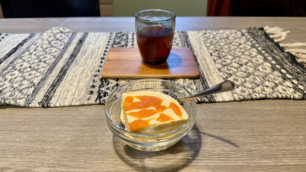 A glass of tea sits next to a dessert in a glass bowl.
