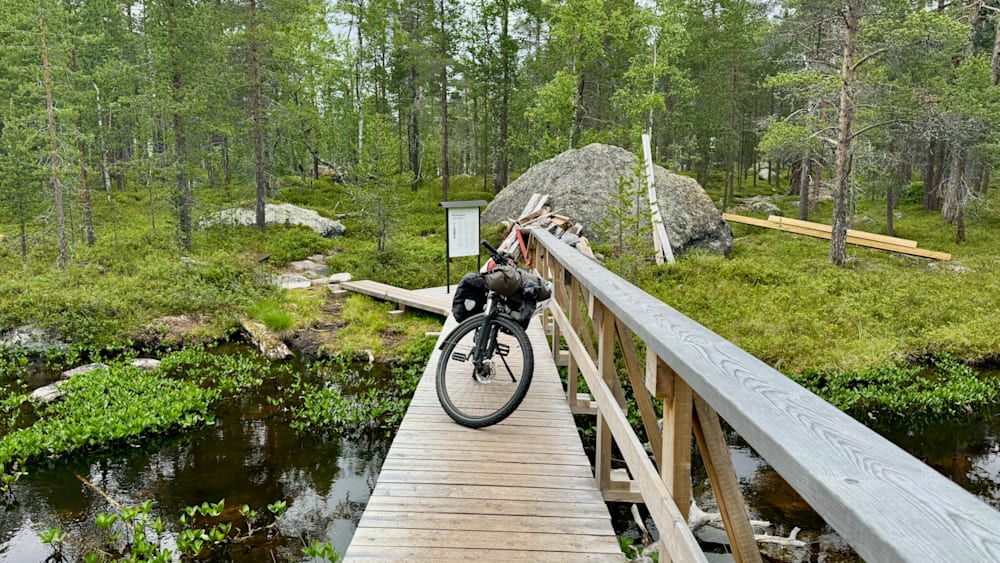A bicycle is parked on a bridge over water with a sign nearby.