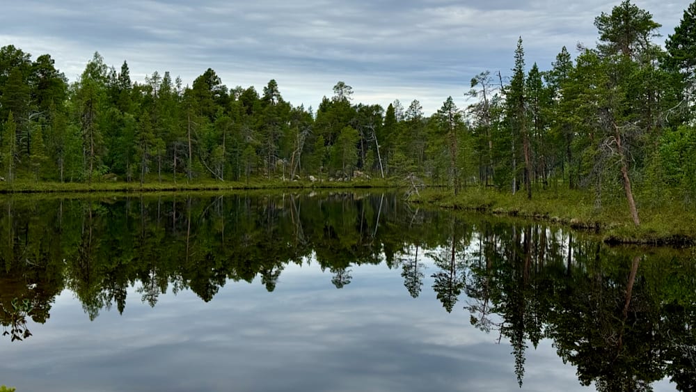 A lake is mirrored in the trees and the sky.