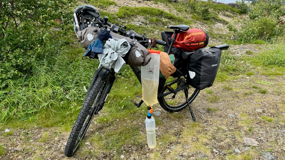 A Ciro hydrant is set up on the side of a bike that is parked on a grassy area.