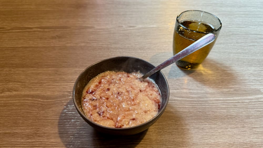 A bowl of cereal is on a table next to a glass of milk.