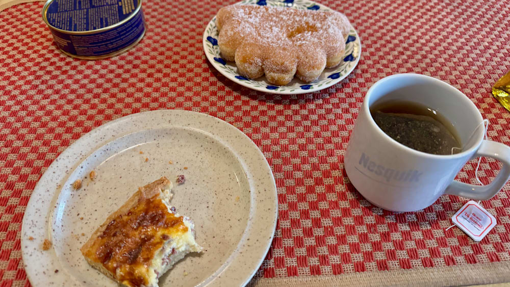 A pastry and coffee set on a table with a plate of doughnuts nearby.