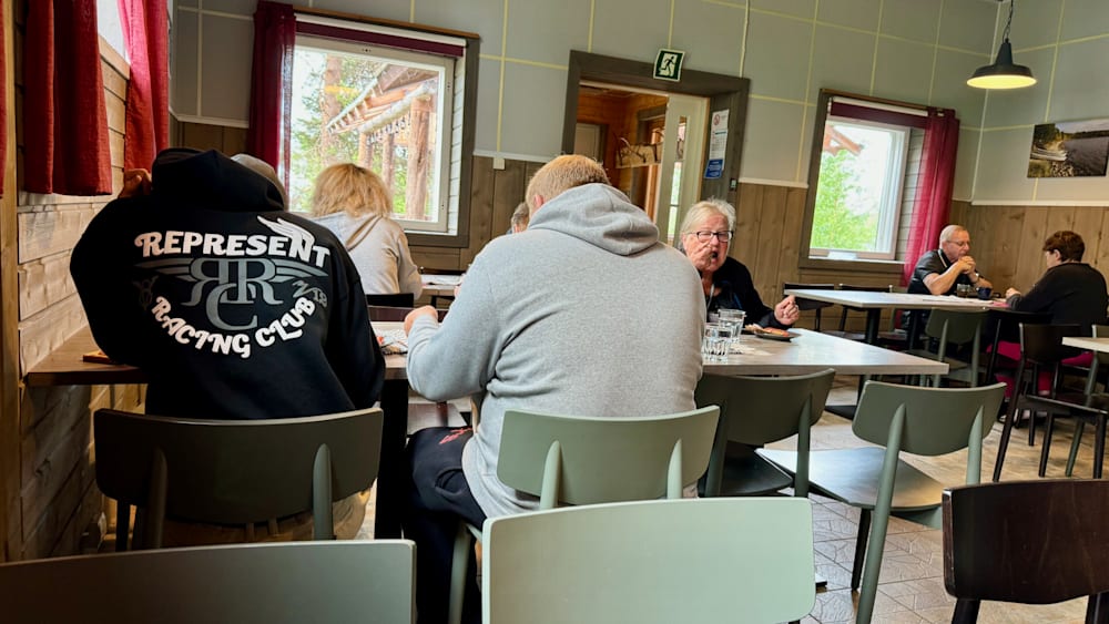 People sitting at a table in a restaurant with a man wearing a sweatshirt that says "present".