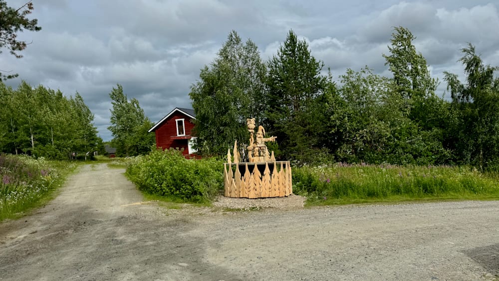 A wooden structure in a field next to a red barn.