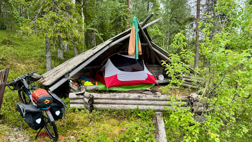 A tent is set up in a wooded area with two other tents in the background.