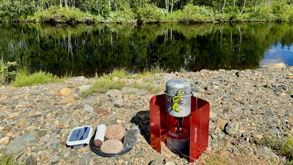 A camping stove sits on some rocks next to some food.