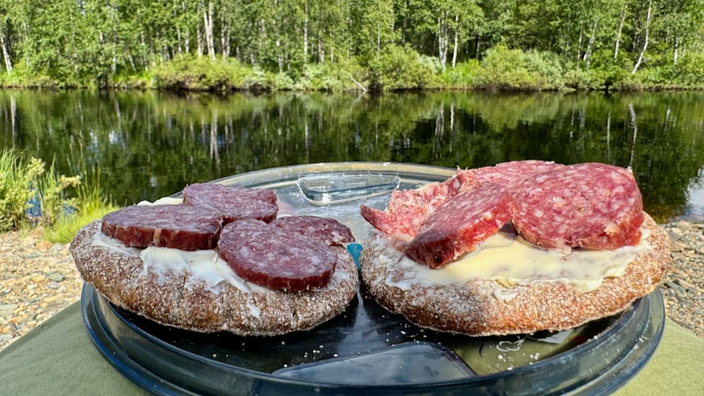 Two slices of pizza are on a plate with a lake in the background.