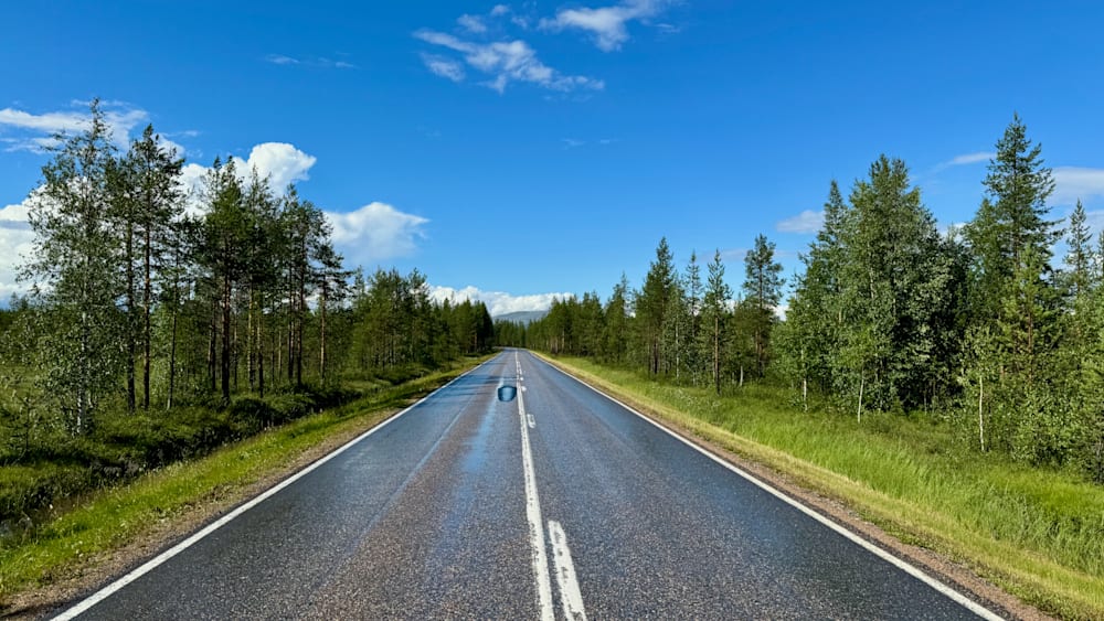 A single vehicle on a road that is wet from rain, with no other cars in sight.