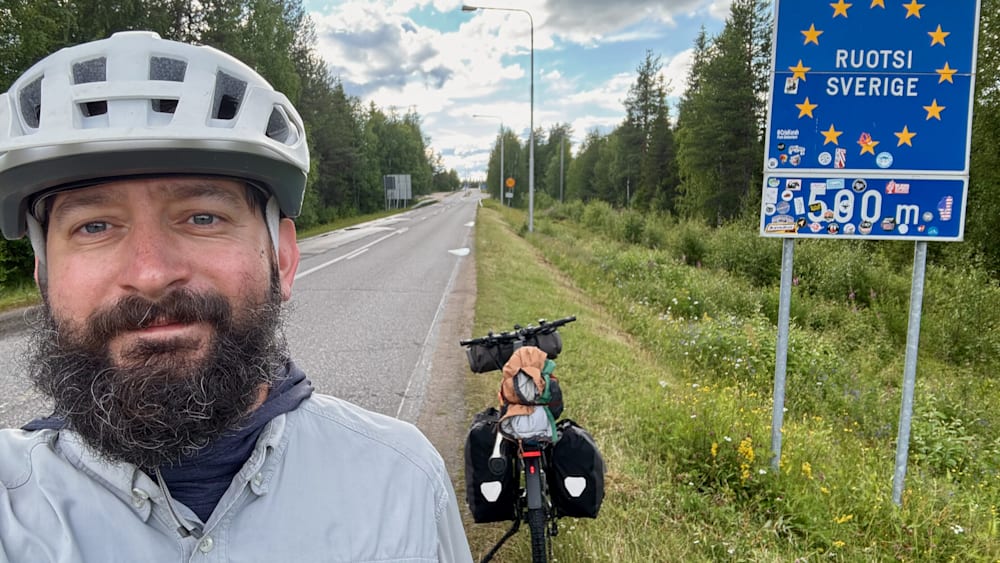 A man wearing a helmet takes a picture of himself with a bike on the side of the road.