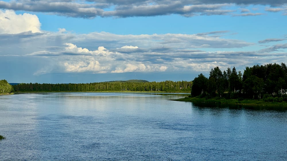 A lake with a forest in the background and a cloud covered sky.