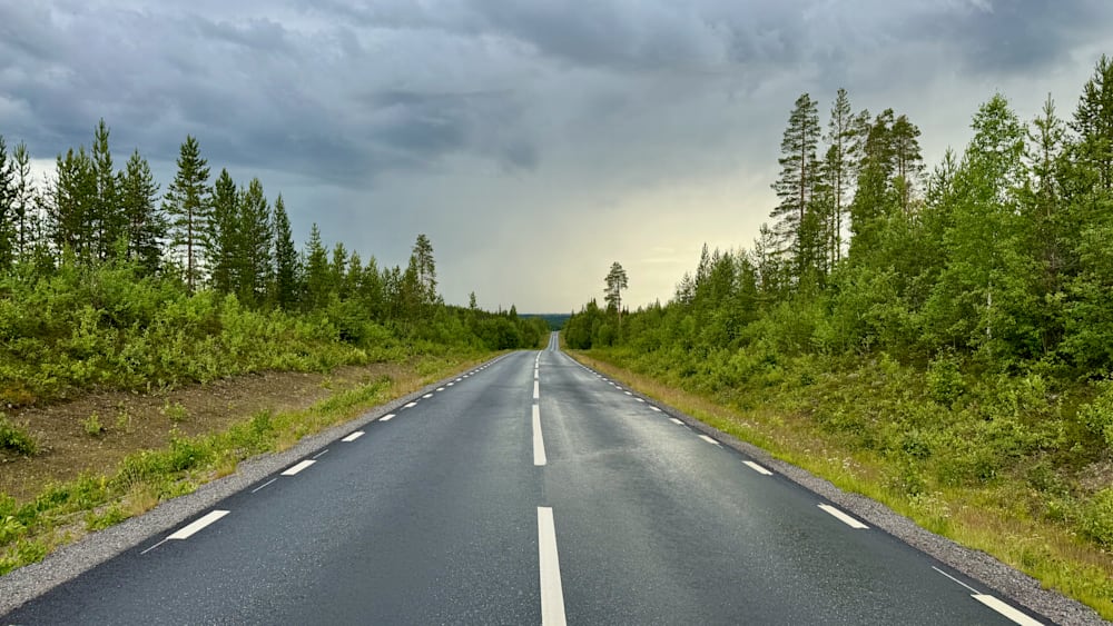 An empty road is depicted with rain in the background.