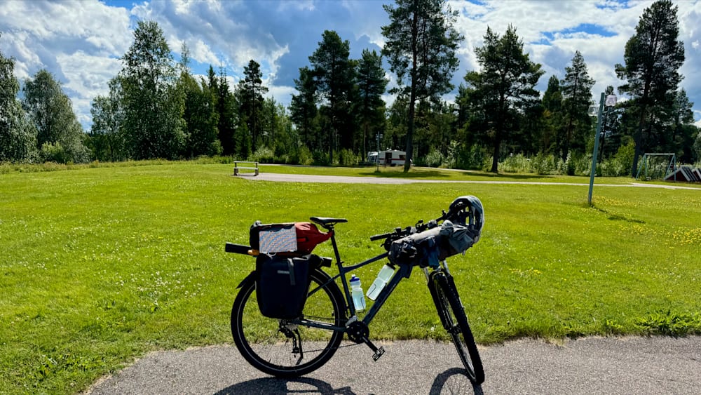 A bicycle with a water bottle on the back is parked next to a bench in a park.