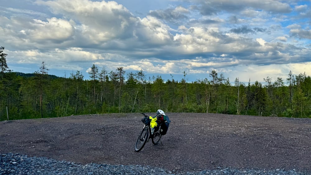A yellow bicycle with a helmet on the back of it is sitting on a gravel lot.