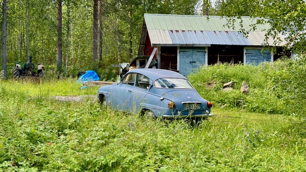 An old blue car is parked in a field with tall grass.