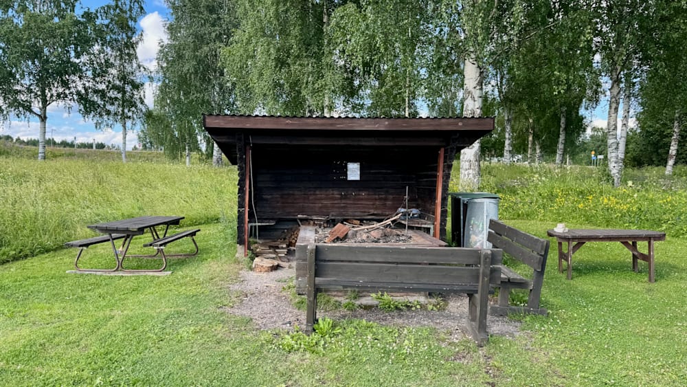 A rustic picnic shelter with a bench and table outside.
