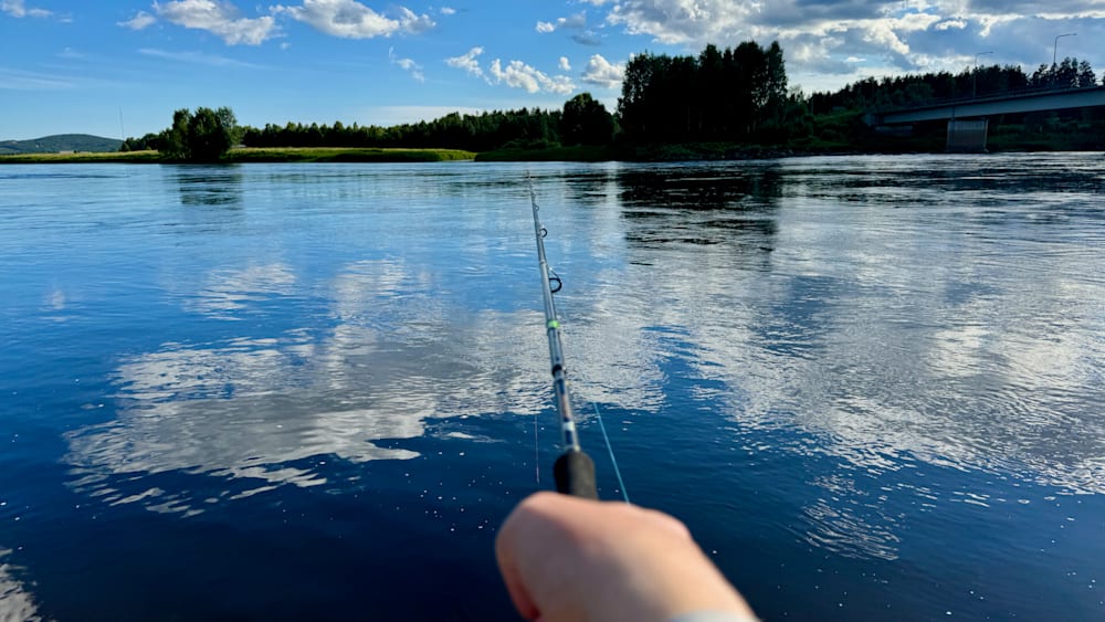 A person is fishing on a body of water with their reflection visible in the water.