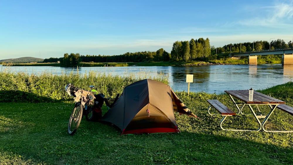 A tent and a bike are set up next to a lake.