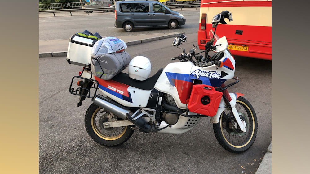 A motorcycle with a red gas tank is parked next to a van.
