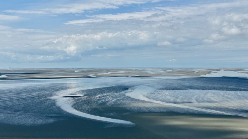 A blue sky and calm waters with no waves in the ocean.
