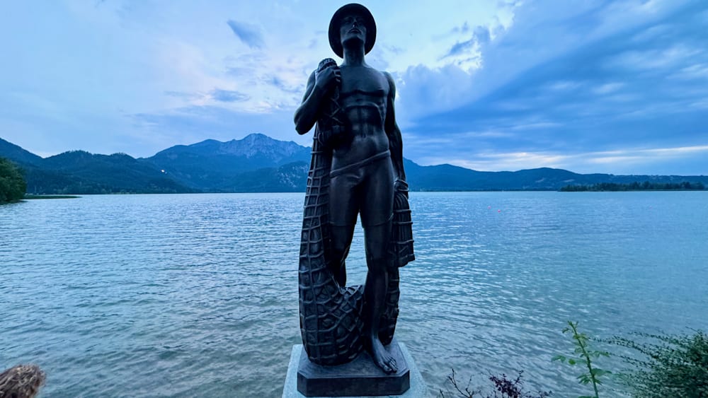 A statue of a man holding a net is in front of a body of water.
