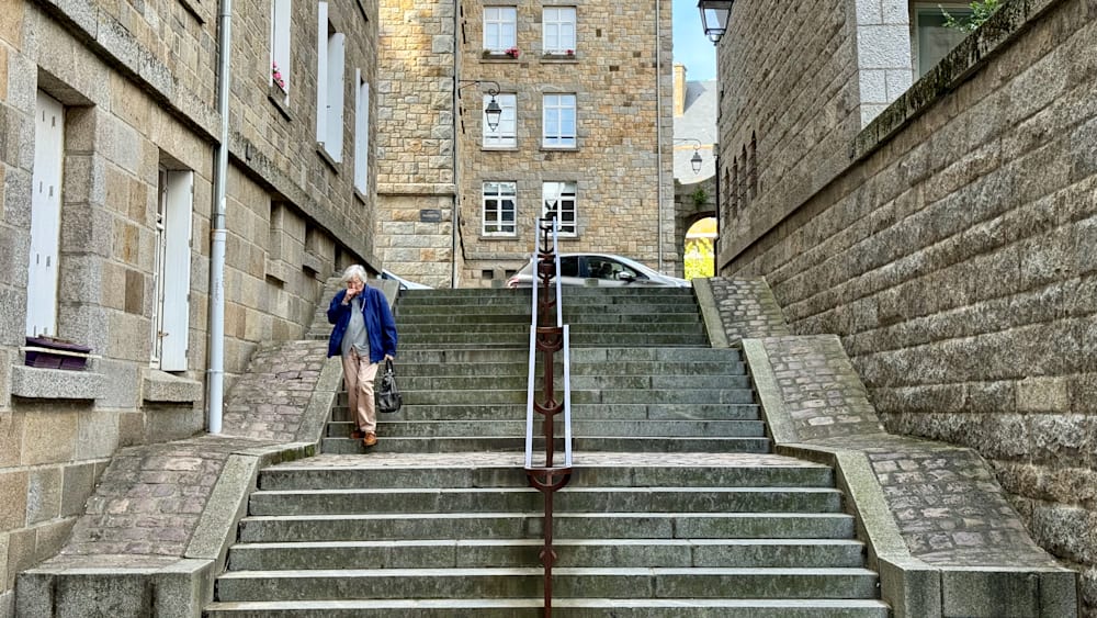 An elderly woman is walking down a set of stairs while talking on her cell phone.