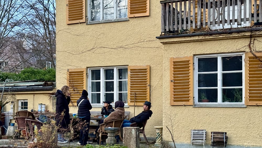 A man wearing a hat is sitting on a chair outside of a house.