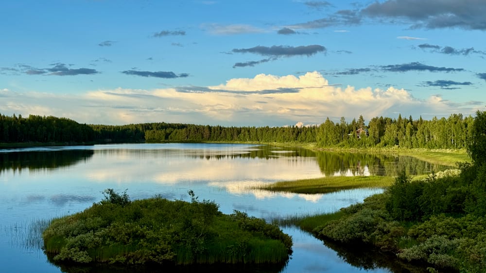 A lake is shown with trees in the background and the water is calm.
