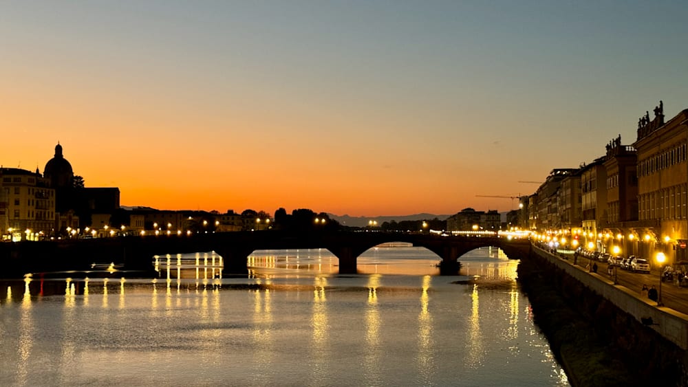 A bridge with lights on it at sunset with water and sky reflection.