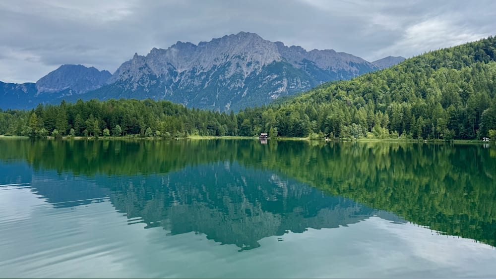 A lake is reflected in a forest and mountains in the background.