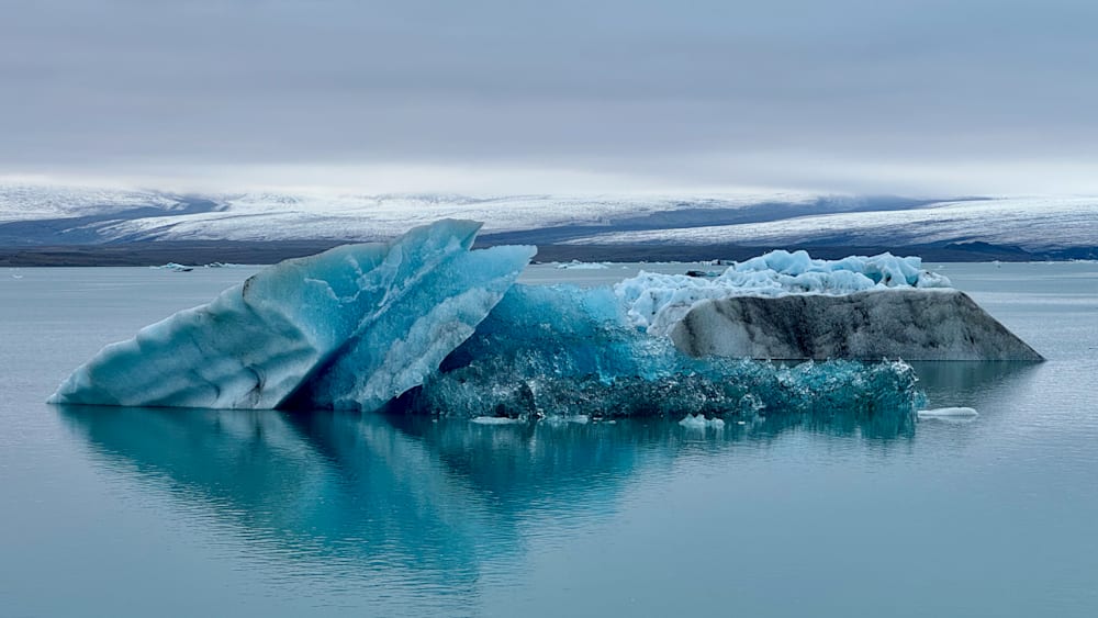 A large block of ice breaks off from a body of water and floats on top.