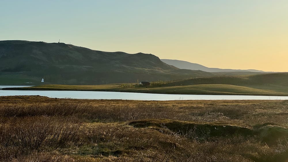 A beautiful view of a lake and mountains with a small cabin in the middle of the wilderness.