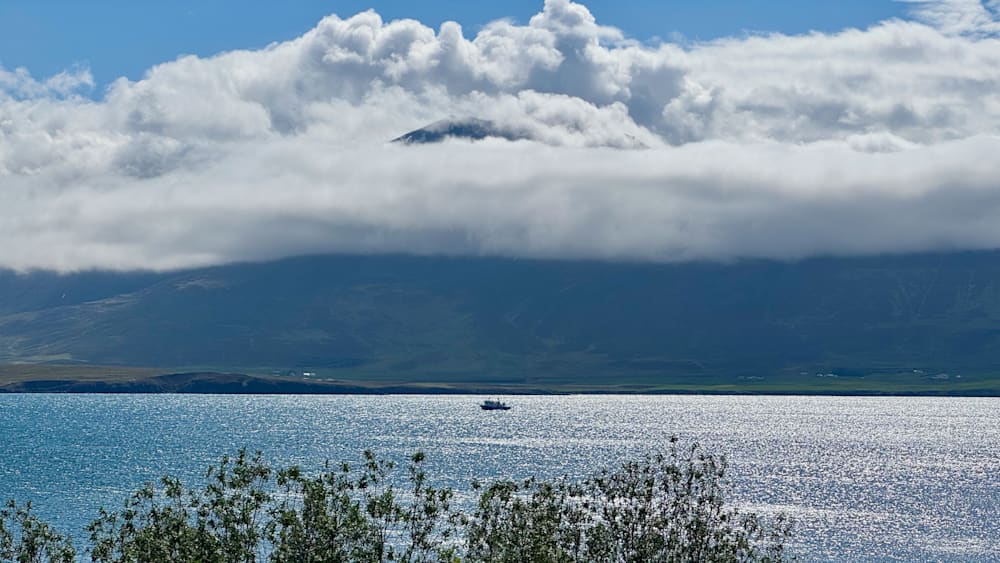 A boat can be seen on a cloudy blue lake with a island in the background.