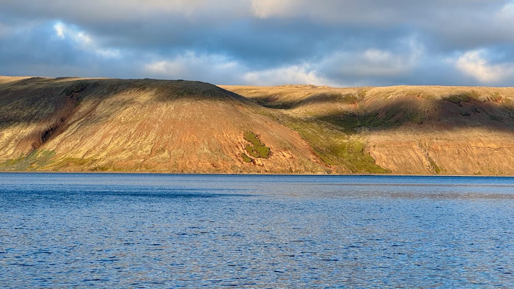A lake with a hill in the background and a cloud covered sky.