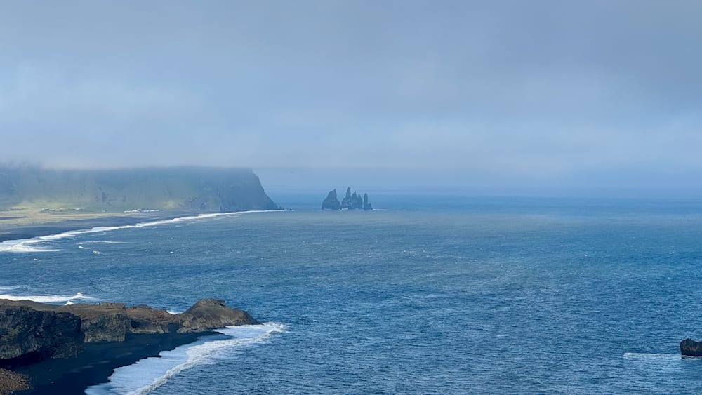 A large body of water with three rock outcroppings in the distance.