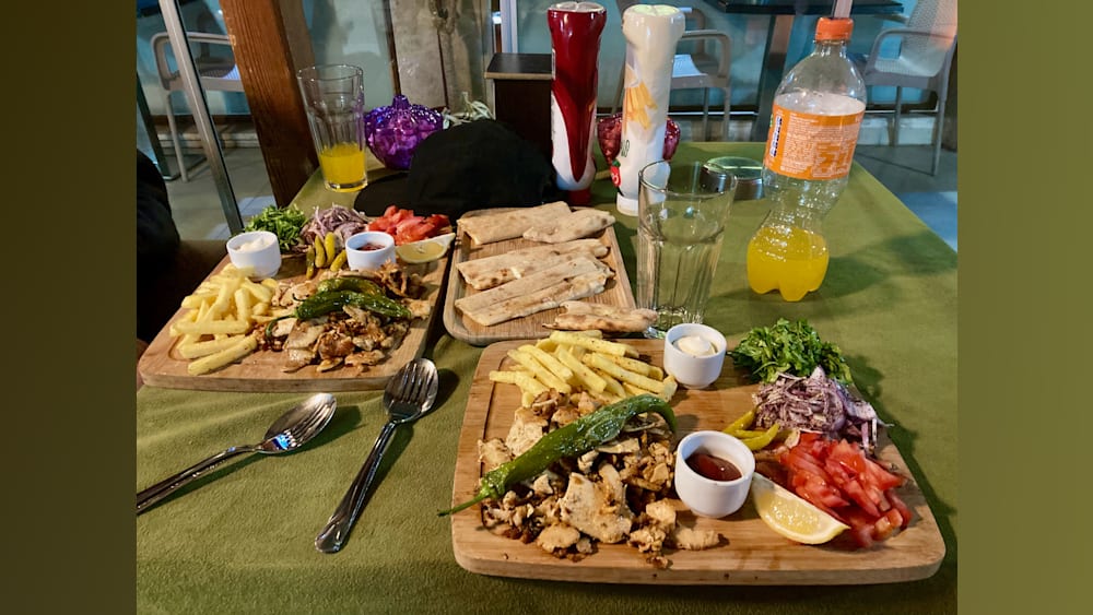 A table with two plates of food and two bottles of drinks.