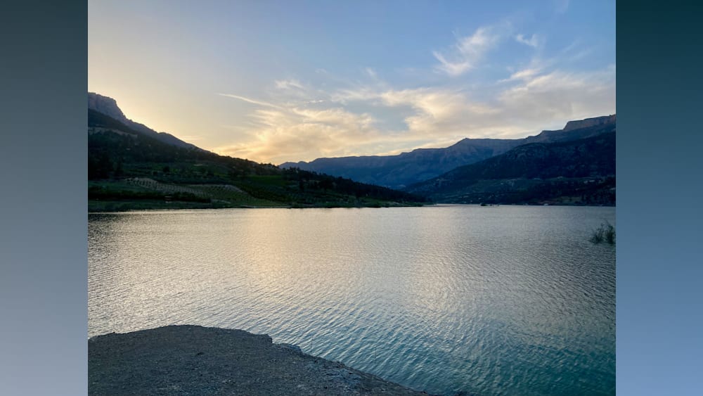 A lake with a mountain in the background is shown with a sunset behind it.
