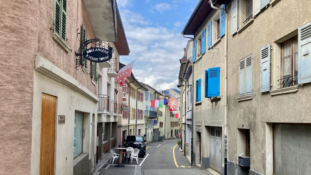 A narrow alleyway between two buildings is lined with tables and chairs on the sidewalk.