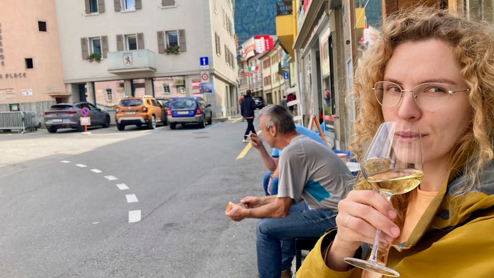 People sitting on a bench by the street with a man eating something off of a plate.