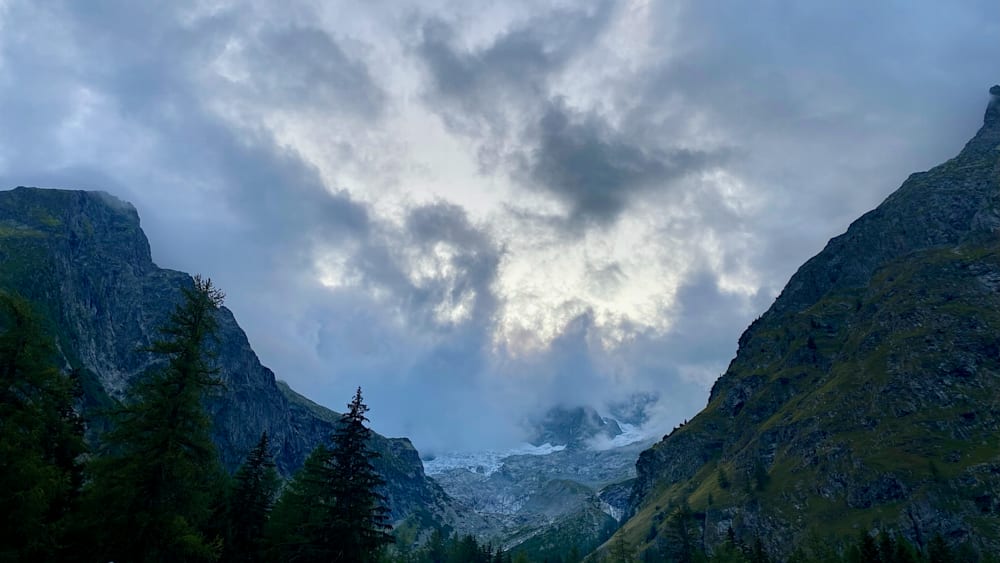 A mountain with a cloud in front of it and a pine tree on the side.