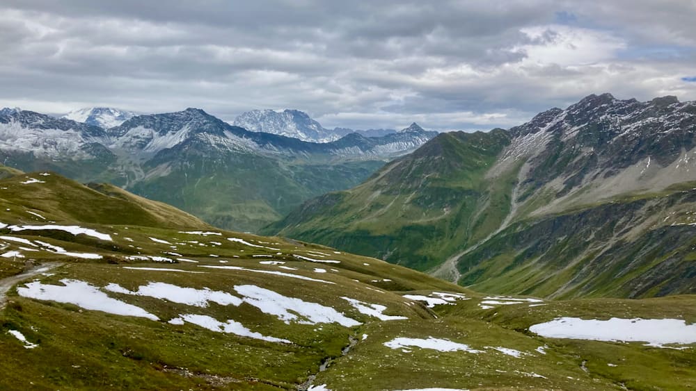 A view of mountains and a valley with snow on the mountains and a stream in the valley.