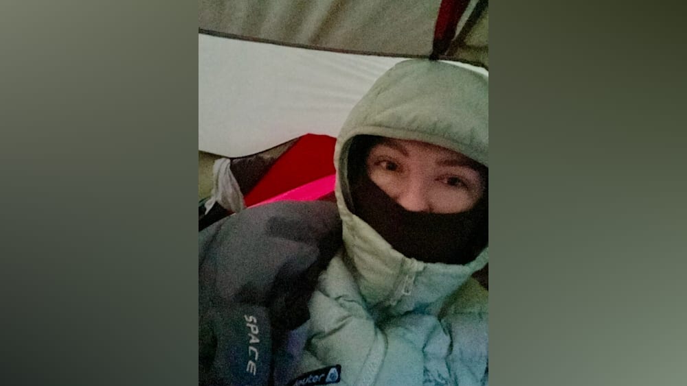 A woman wearing a heavy jacket and a mask covering her mouth and nose.