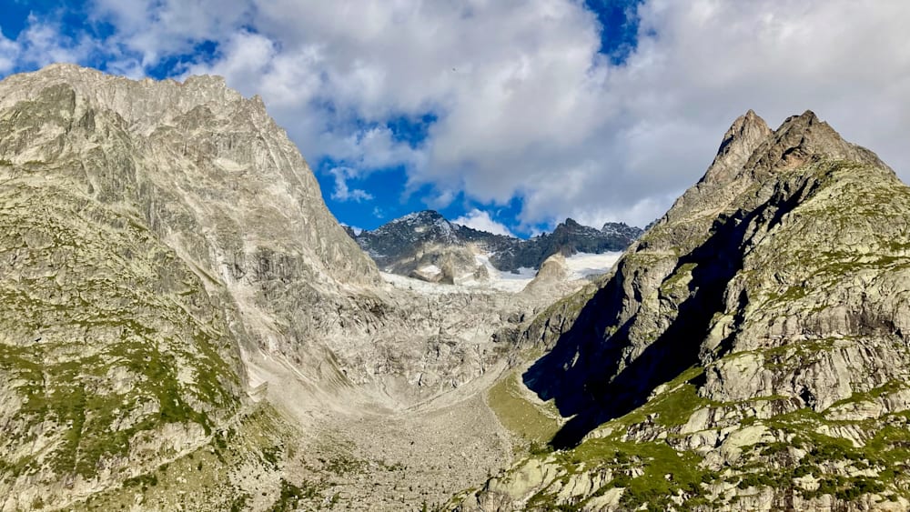 An alpine landscape with a mountain range and a valley between them, with snow on the mountainside.