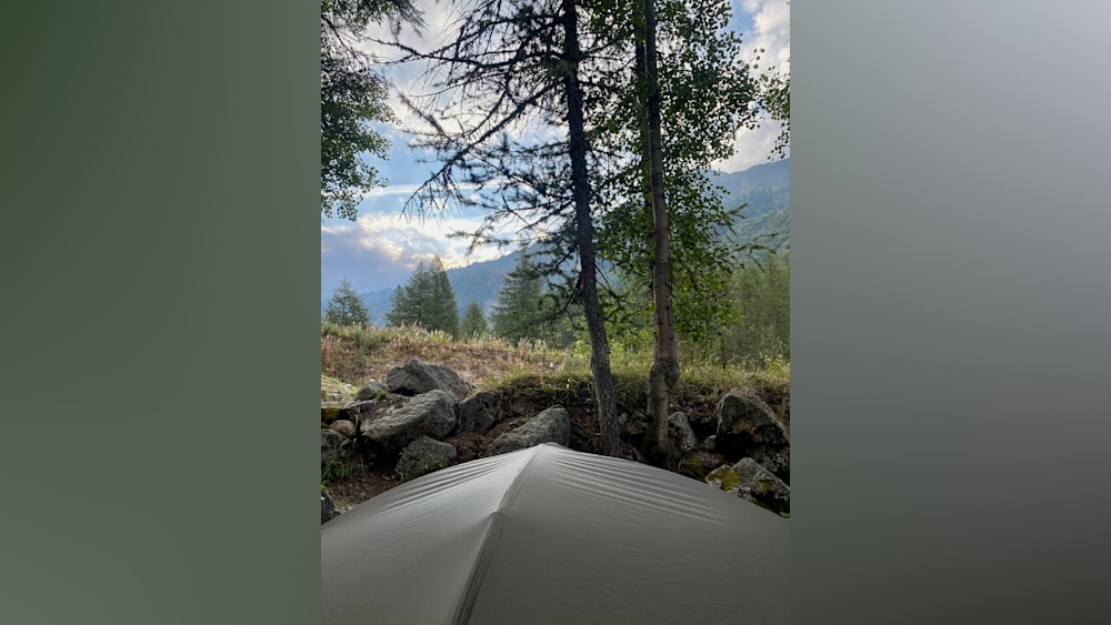 A tent is pitched in a wooded area with boulders and trees in the background.