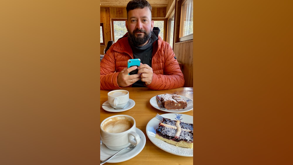 A man wearing an orange jacket is sitting at a table looking at his phone.
