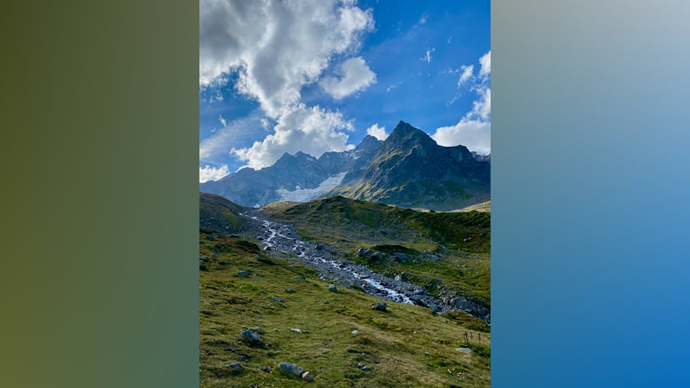 A stream runs down a mountainside surrounded by grass and rocks.