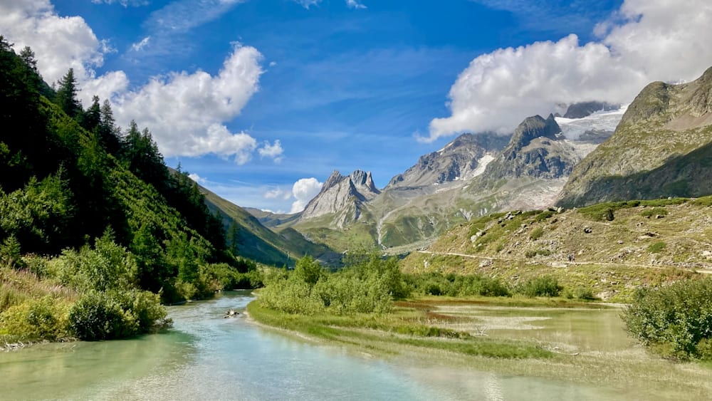 A mountain stream with trees and a blue sky in the background.
