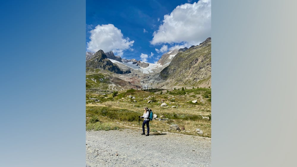 A woman standing on a mountain with a blue backpack on her shoulders.
