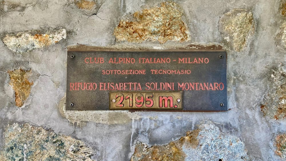 A sign that says Club Alpino Italy/Milano on it with numbers 21975m in red.